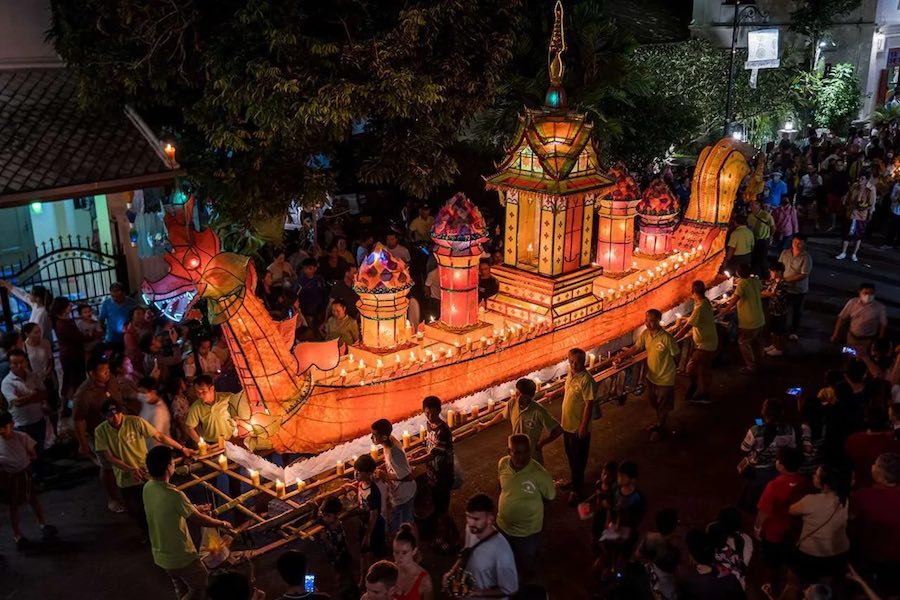 Persone che portano barche di lanterne e accendono candele per le strade di Luang Prabang, in Laos